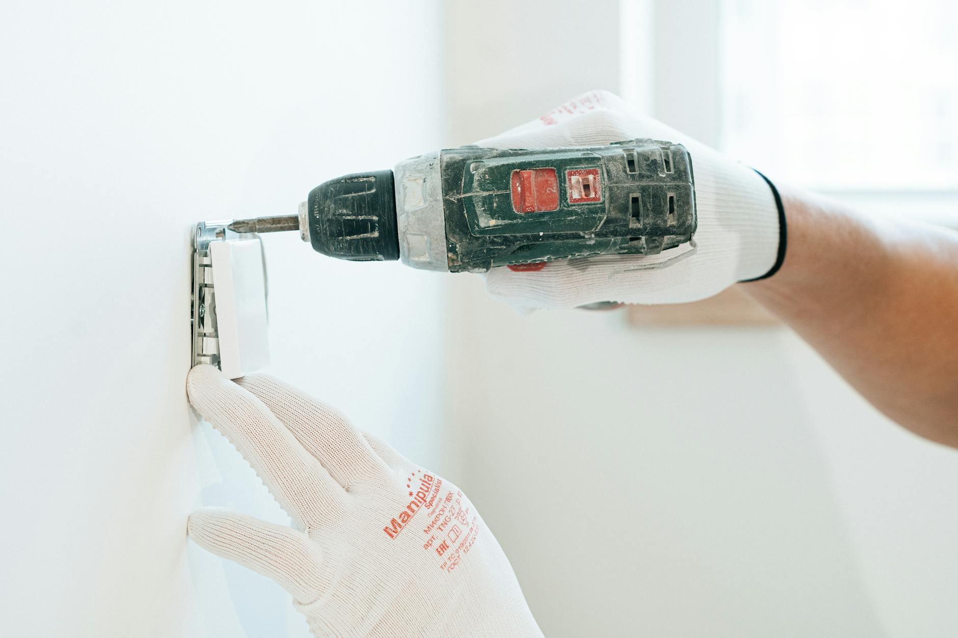 Elektryk w rękawicach montuje gniazdko w ścianie w trakcie remontu