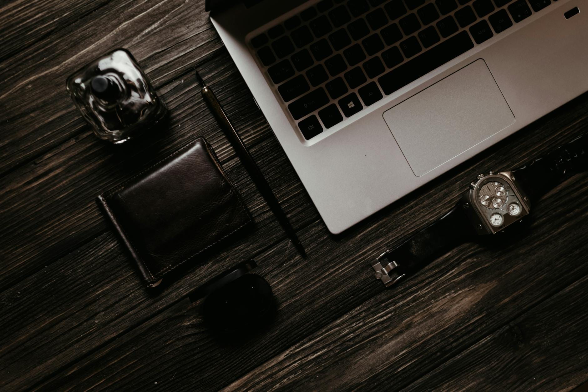 Perfumy, laptop i akcesoria biurowe ułożone na drewnianym blacie