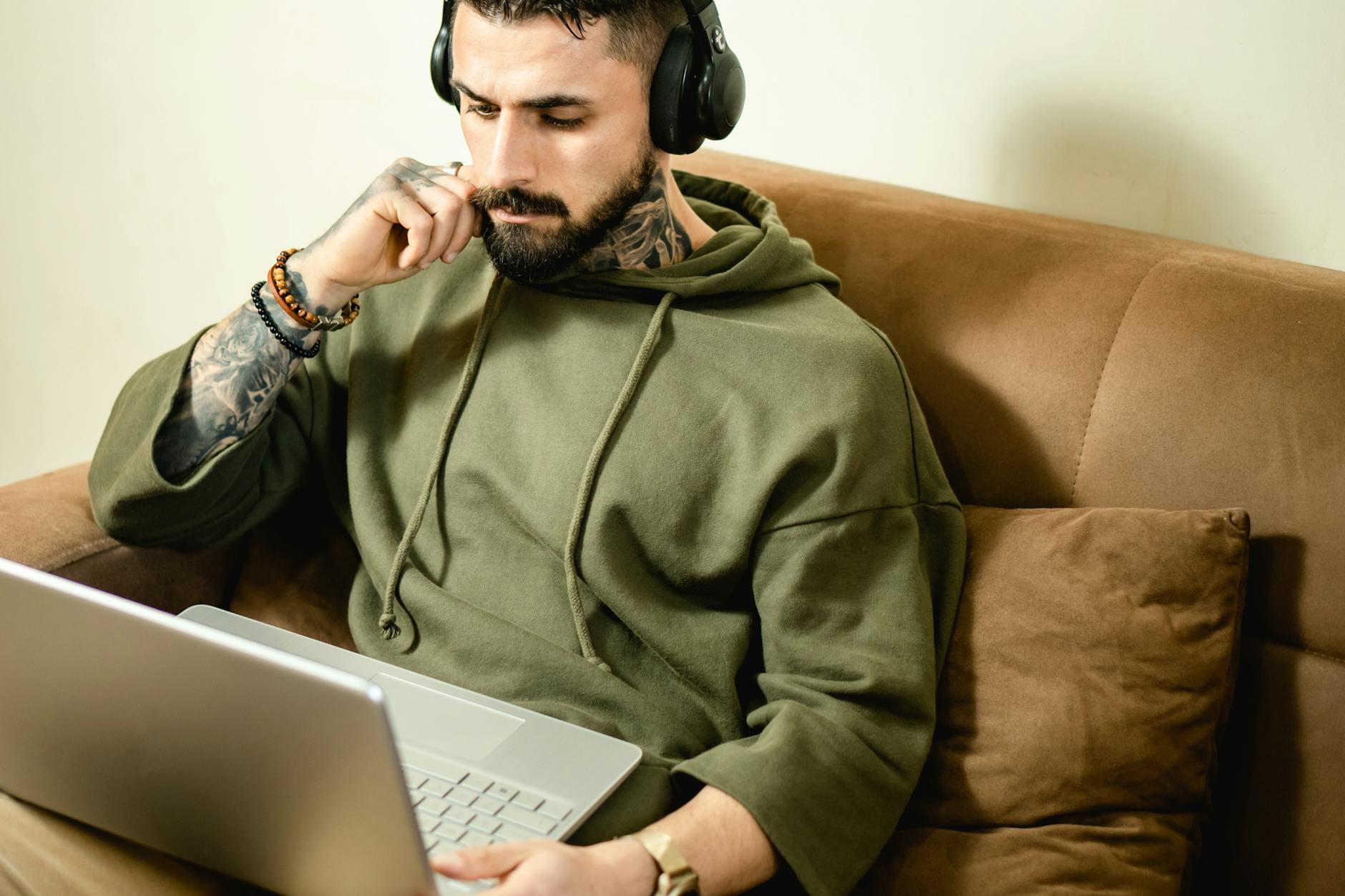 Wytatuowany mężczyzna w słuchawkach pracuje z domu przy laptopie
