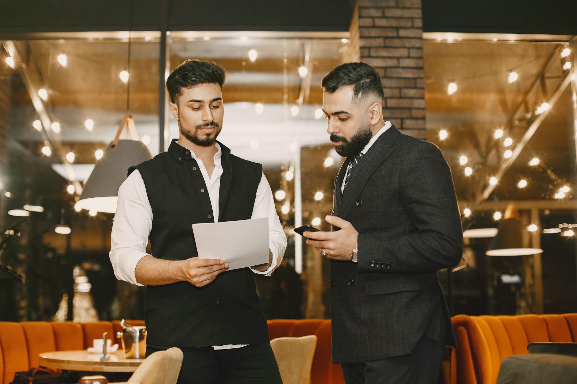 Dwóch biznesmenów przy stoliku w restauracji przegląda telefon i dokumenty