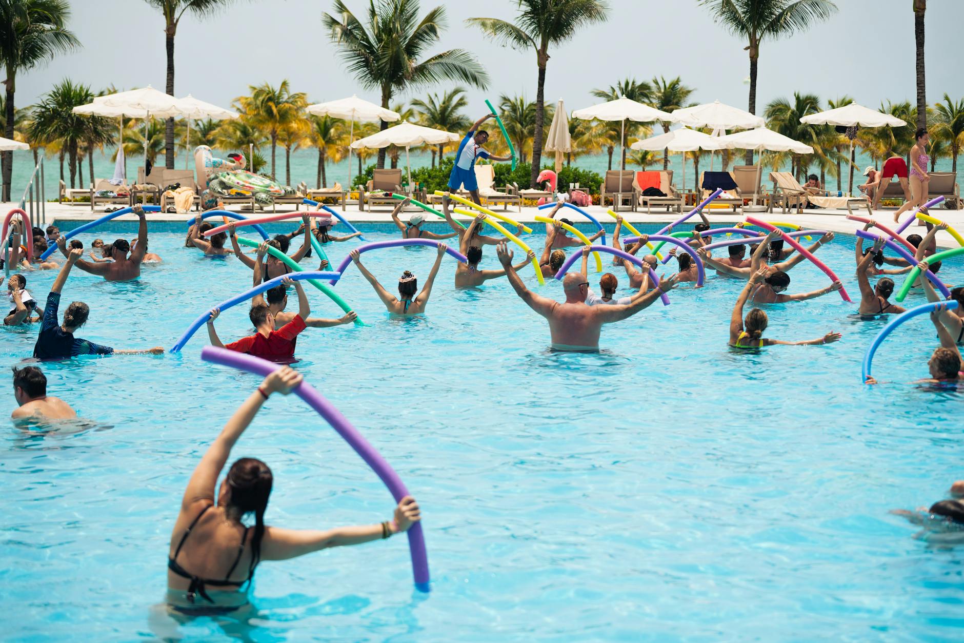 Grupa ćwicząca aqua aerobik z makaronami w hotelowym basenie w tropikach