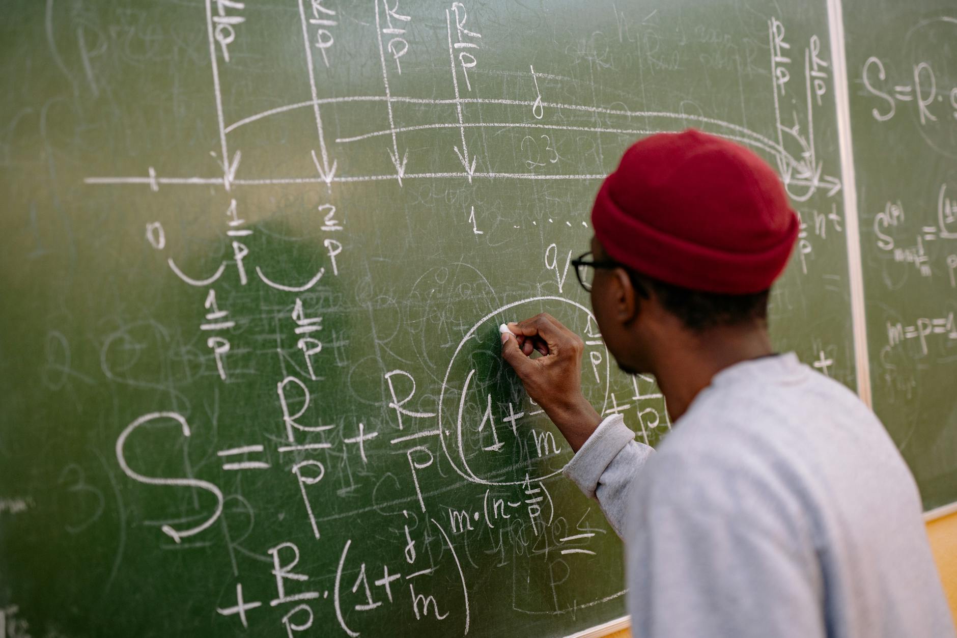 Uczeń zapisuje złożone równania matematyczne na tablicy w klasie