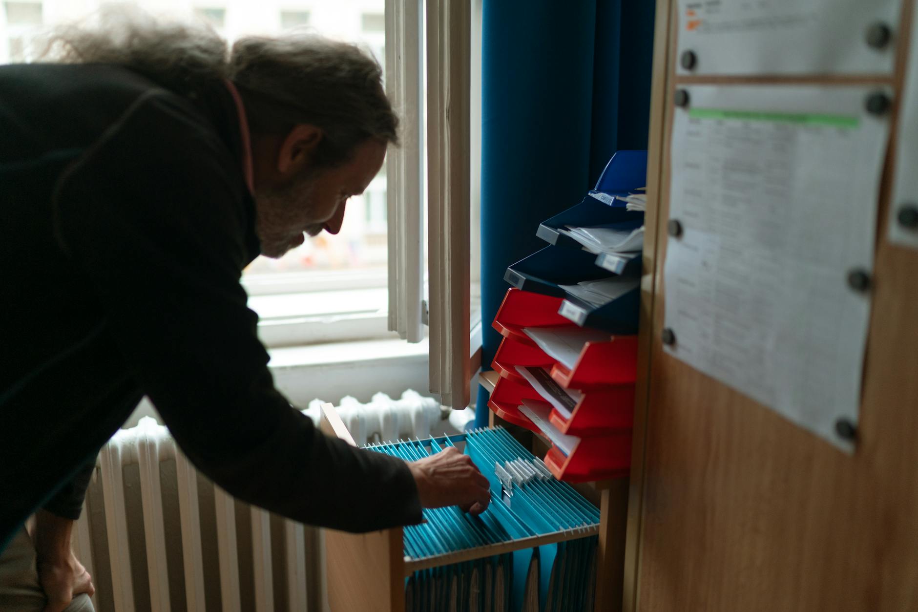 Mężczyzna z długimi włosami przeszukuje dokumenty w uporządkowanym biurze