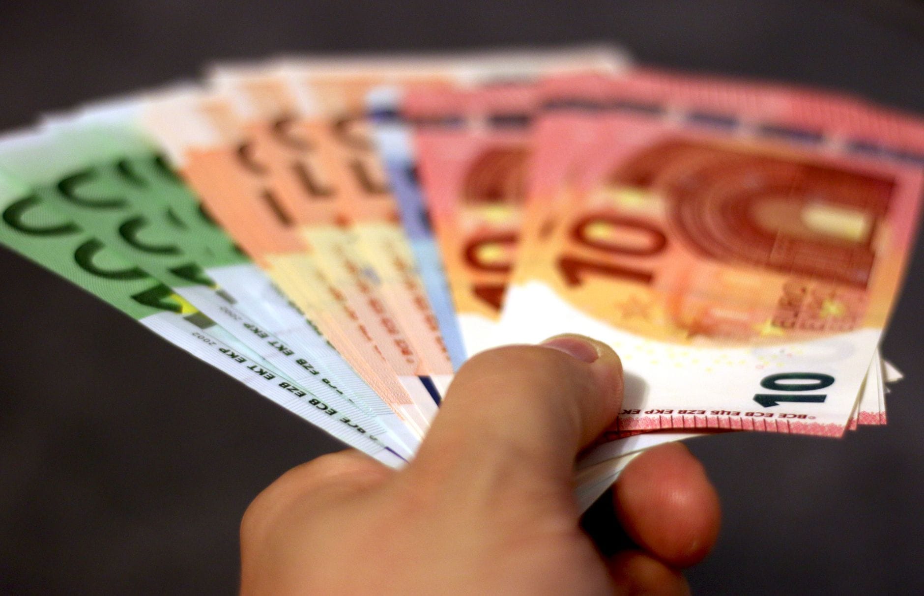 Dłoń trzyma wachlarz banknotów euro symbolizujących fundusze unijne