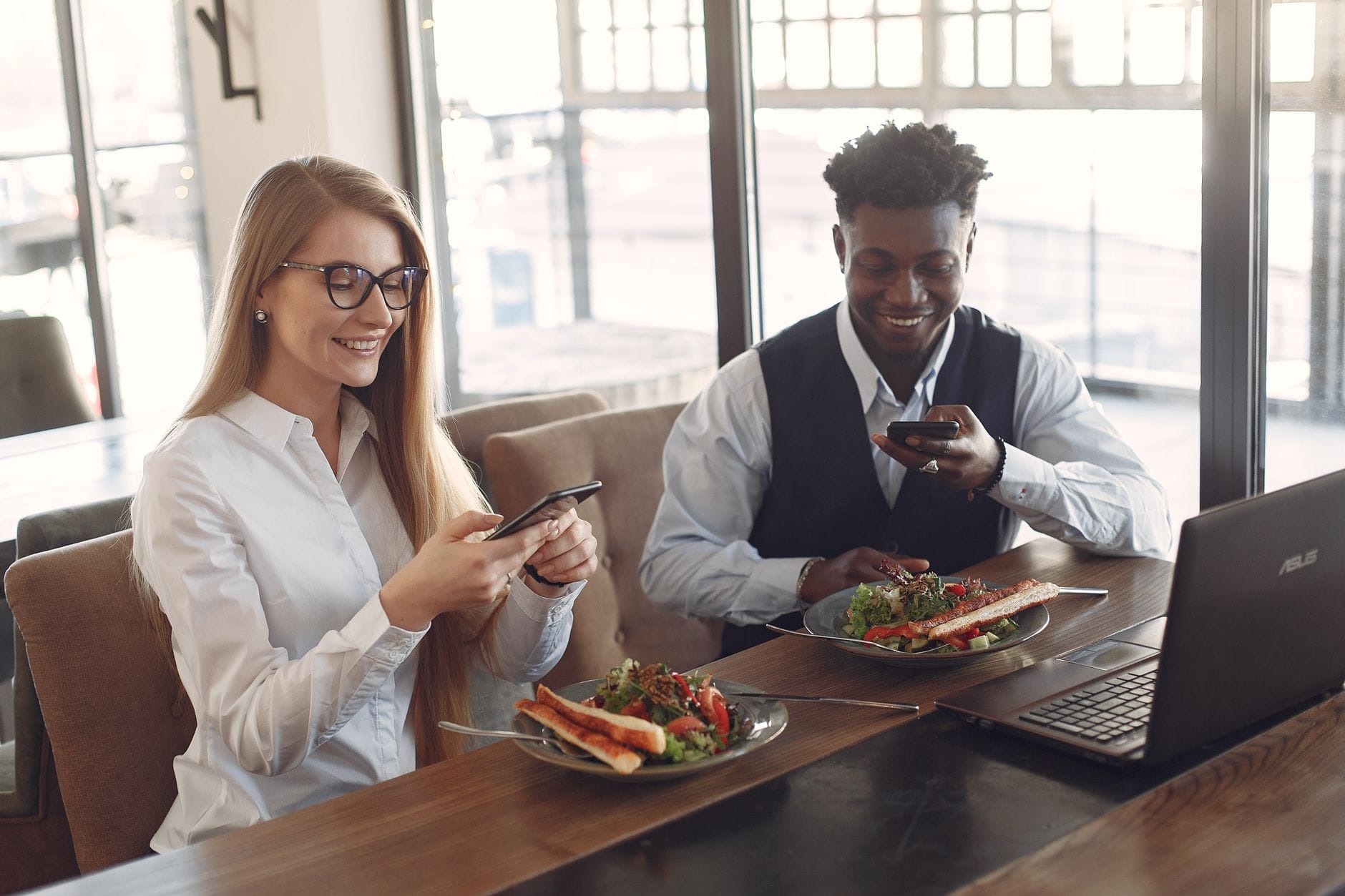 Młodzi pracownicy przy lunchu w kawiarni przeglądają smartfony